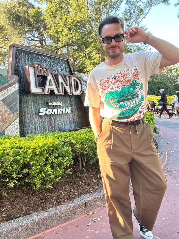 man with sunglasses wearing the landscapes of tomorrow tee in front of The Land ride at Epcot